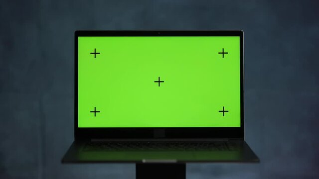 Laptop with a green screen and tracking points stands on a blue marble background and rotates