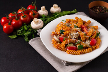 Vegetarian fusilli pasta with zucchini, tomatoes and mushrooms, in a white plate, on a gray background