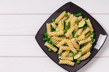 Vegetarian fusilli pasta with zucchini and peas, in a gray plate, on a wooden background