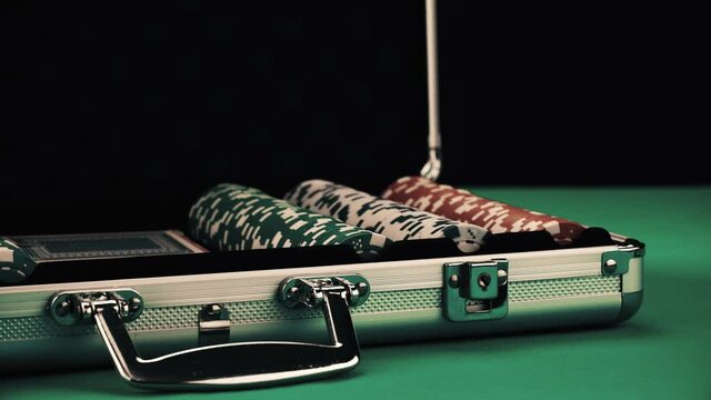 Opening a metal suitcase with poker equipment on a green table and black background. There are chips and cards. Concept of playing hazard games in a casino. Gambling as entertainment at leisure time.
