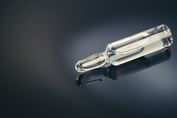 medicine glass ampoule with transparent liquid at it over dark blue gradient background. copy...