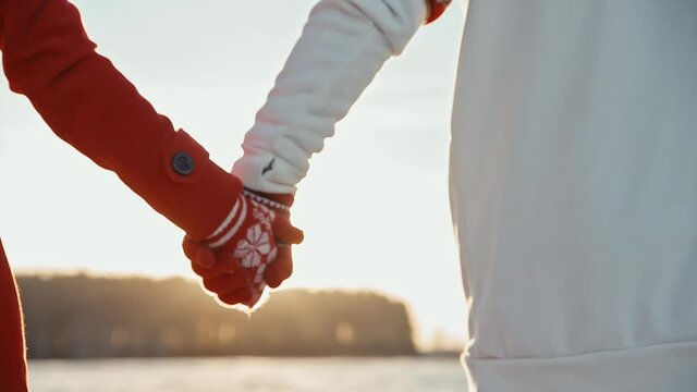 Back view of couple holding hands wearing gloves at winter sunset. Two people on date during xmas time. Love and relationship concept.