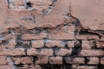 Old brick wall with peeling stucco. Weathered rough wall surface with brickwork. The wall is painted in different colors. Vintage background. Urban texture.