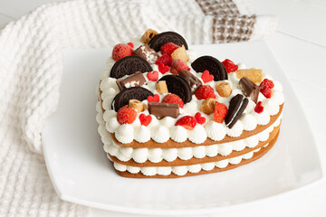 Heart-shaped cake with ricotta and whipped cream, decorated with chocolate, waffles, cookies and strawberries
