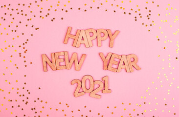 Lettering on a pink background of wooden letters Happy New Year 2021 surrounded by gold stars.