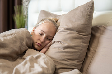 Teenage girl with blond hair sleeps in brown bed