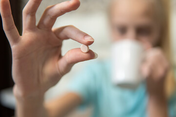 The girl holds the pill and drinks medicine. close-up