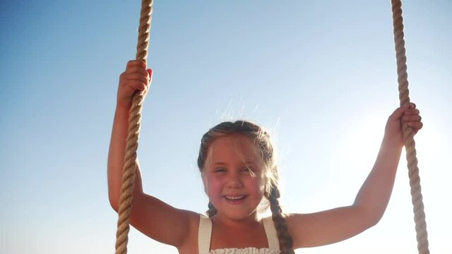 little girl kid swinging on a wooden swing on a tree in the park. happy family kid dream concept. little fun kid girl playing on wooden swing on tree fun dream concept in park