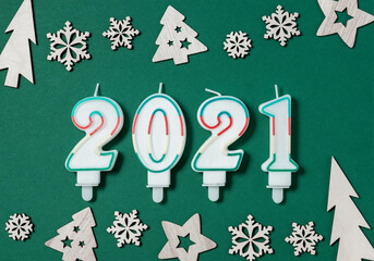 2021 year flat lay composition. Candles in shape of figures, border made of wooden Xmas decorations up and down on green background. Happy New year greeting card concept. Top view.