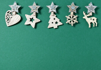 Christmas minimal flat lay composition. Border made of wooden Xmas decorations in shape of stars, xmas tree, snowflake and deer on green background. New Year, winter holidays. Top view, copy space.