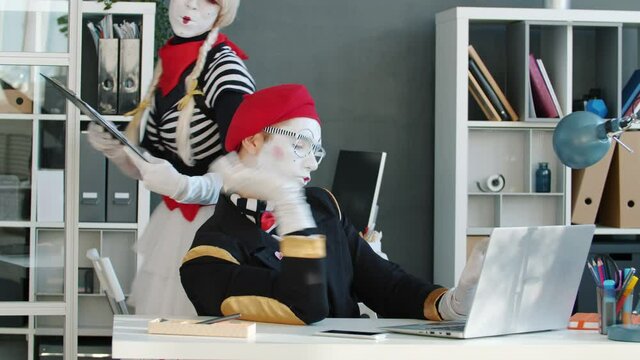 Mime CEO in funny costume is talking on mobile phone working with laptop signing papers for secretary in office. Business activities parody concept.