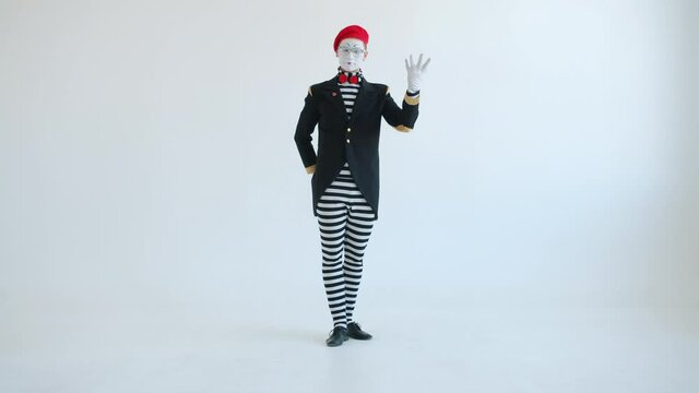 Funny pantomimist is showing creative tricks with football looking at camera moving against white background. Sports and comic actors concept.