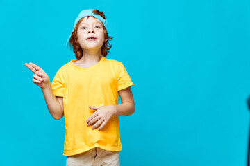 Red-haired boy showing toes yellow t-shirt blue cap studio isolated background 