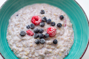 Oatmeal porridge in a plate with currant and raspberry berries.