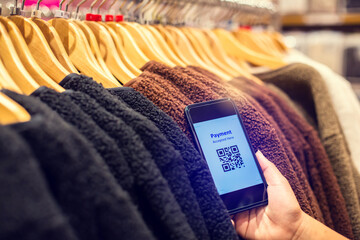 Selective focus to payment QR code tag on smartphone with blurry many clothes in the store to accepted generate digital pay without money. Qr code payment concept.