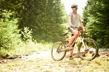 Obraz premium Young male cyclist riding in the mountain forest against the background of mountain fir trees at sunset.