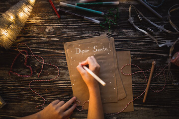Children's hands write Dear Santa, Child writes a Letter to Santa Claus on craft paper, top view,...