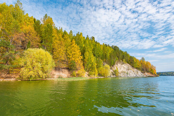 Autumn forest trees are reflected in the river water of the panoramic landscape. Blue sky with clouds.