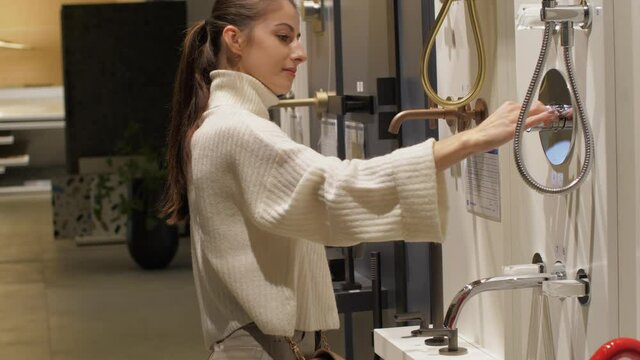 Professional designer with long hair in ponytail looks at different taps on wall of local hardware store. Concept apartment renovation