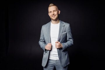 Photo portrait of smiling cheerful man in stylish grey suit isolated on black color studio...