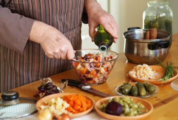 The process of preparing an elderly woman vinaigrette, salad of boiled beets and vegetables, on a wooden natural table. Diet, vegan natural healthy food.