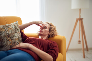 Woman with sinus pain, headache and stomach problems, lying on a couch at home.