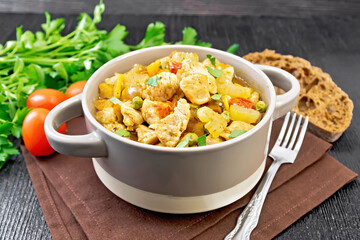 Chicken with vegetables and peas in saucepan on dark board
