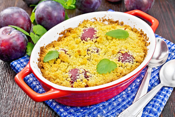 Crumble with plum in brazier on dark board
