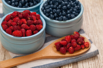 Blueberries and strawberries in blue bowls on white wooden background, organic food concept