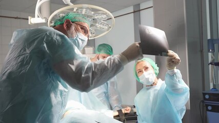 Medical workers in hospital examine x-ray prints during operation, caucasian medics consult with each other while looking at x ray image, medicine, surgery, healthcare concept. - Powered by Adobe