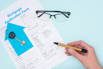 Hand holds a pen over a mortgage application form for the purchase of a house or apartment, key, glasses