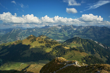 Aerial panoramic view of beautiful countryside with green hills and mountain ranges in the background and cloudy blue sky above on a sunny day in Chur, Switzerland.