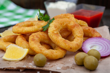 Deep fried squid or fish rings appetizer. Breaded squid or fish rings with lemon,  ketchup and tartar sauce. Close up of golden, crispy calamari snack.