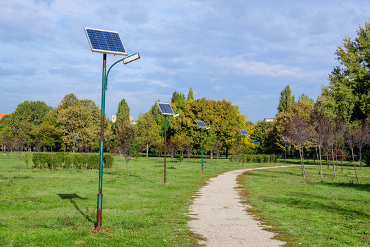 Long alley and many lighting poles activated with attached blue solar panels in Parcul Izvor (Izvor Park) in Bucharest, Romania, with cloudy sky in the background, in a summer day.