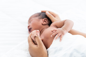 Fototapeta na wymiar Top view of African American newborn baby or infant lying on white bed while mother’s hands takes care and comforting. Family, love and new life concept