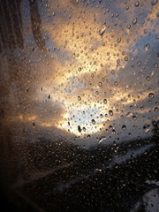 Vertical close-up view of water droplets on a glass window in winter, with snow covered mountains near sunrise outside