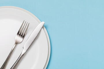 White ceramic plate and cutlery on a blue background with copy space. Food background