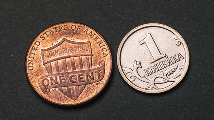 One Russian kopeck and an American cent on a dark background