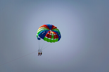 A rainbow-colored striped parachute with two passengers under it. People flying over the blue sea. Entertainment at the resort and active recreation on vacation and on vacation