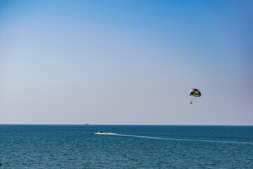 Fototapeta na wymiar A rainbow-colored striped parachute with two passengers under it. People flying over the blue sea. Entertainment at the resort and active recreation on vacation and on vacation