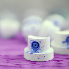 The soiled blue nozzles from the paint sprayer lies on a purple plank on a background of a many...