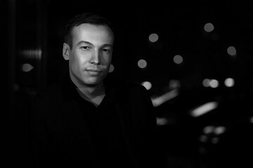 Obraz na płótnie Canvas Beautiful young guy on a dark blurred background , black and white photo
