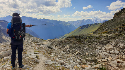 Obraz premium A man pointing with hiking stick in direction if Gro?glockner, while hiking in Heiligenblut region in Austria. There are many high chains of Alps behind him. Narrow pathway. Looking for directions