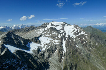 Panoramic view from top of Hohe Sonnblick in Austrian Alps on Gro?glockner. The whole area is partially covered with snow, lush green meadows below. Many mountain chains in the back. Sunny day.