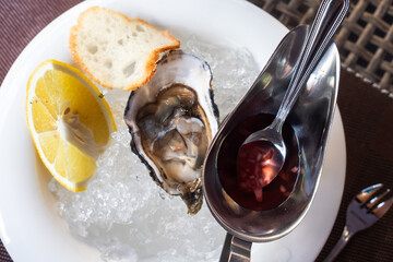 One oyster, a gravy boat with sauce and a slice of lemon.