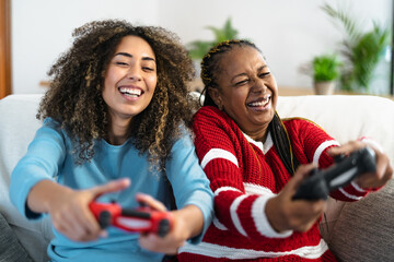 Happy mother and daughter having fun playing video game at home - Gaming entertainment and...