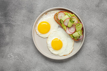 Healthy breakfast - a sandwich with avocado, cucumber and radish and fried eggs on a table
