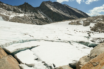 Obraz premium A footprints on the snow, lying on a glacier under Hohe Sonnblick in Austrian Alps. The footprints lead in one direction. Many high mountain peaks. Clear and sunny day. Creeks on the glacier