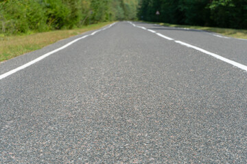 Empty asphalt road through woods and fields. New fresh asphalt pavement away from the city. Development of rural infrastructure. Road marking lines close up.