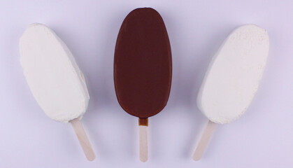 Two white and one chocolate ice cream on a stick on a white background
